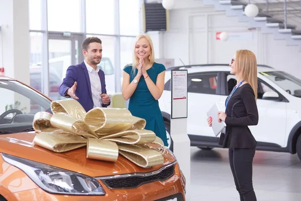 Een man maakt een geschenk - een auto aan zijn vrouw. Ze is hier verbaasd over. Ze zijn hier erg blij mee. — Stockfoto