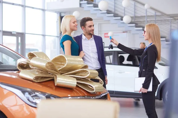 Een man maakt een geschenk - een auto aan zijn vrouw. Ze is hier verbaasd over. Ze zijn hier erg blij mee. — Stockfoto