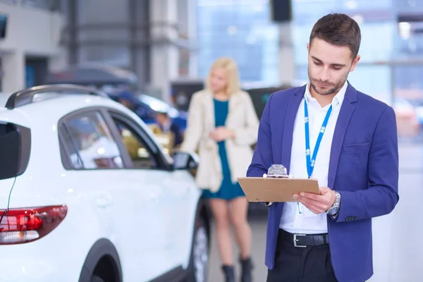 Negociante com mulher fica perto de um carro novo no showroom — Fotografia de Stock