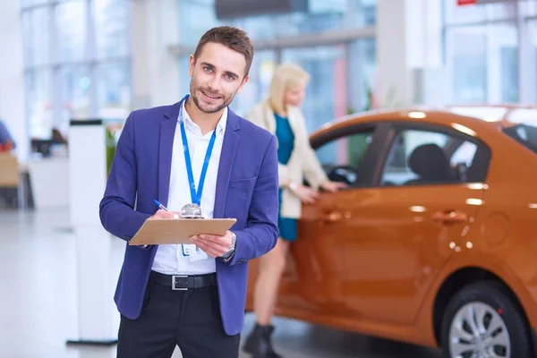 Vendedor fica perto de um carro novo no showroom — Fotografia de Stock