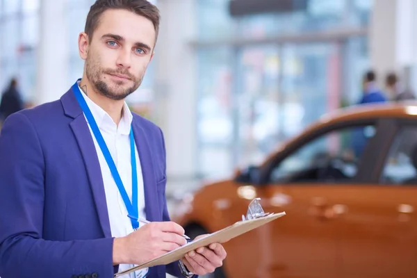 Vendedor fica perto de um carro novo no showroom — Fotografia de Stock