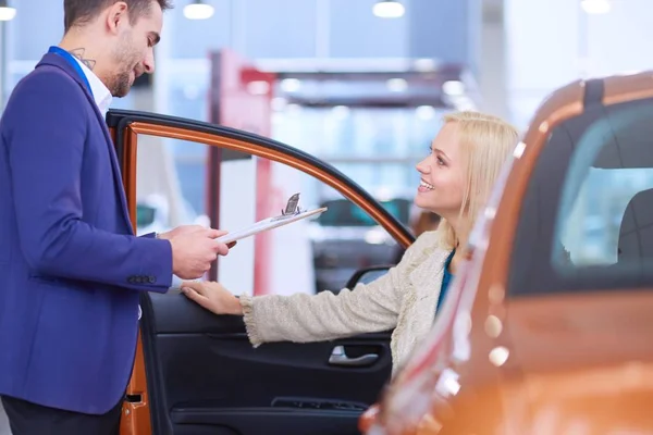 Negociante com mulher fica perto de um carro novo no showroom — Fotografia de Stock