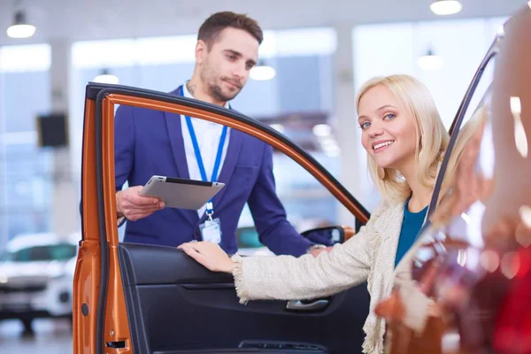 Distribuidor de mujer se para cerca de un coche nuevo en la sala de exposición — Foto de Stock