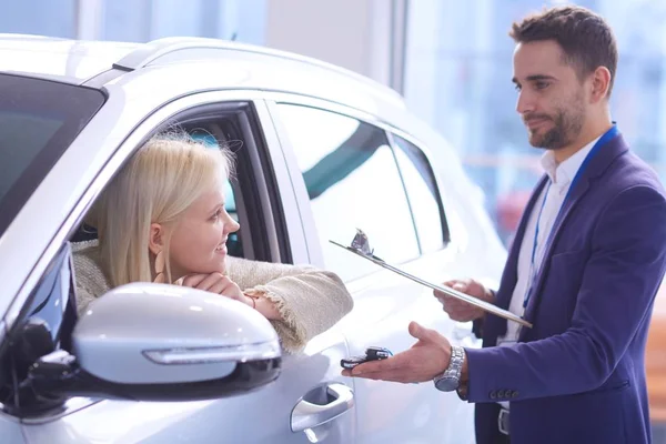 Vendedor de coches vende un coche a cliente feliz en concesionario de coches y las manos sobre las llaves — Foto de Stock