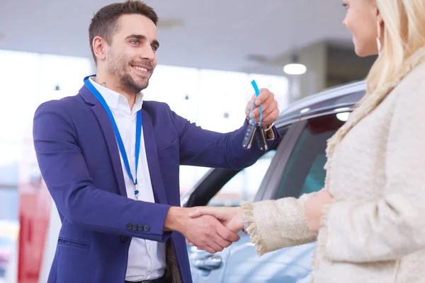 Imagen del saludo del concesionario de coches con la mujer feliz en el centro del automóvil — Foto de Stock