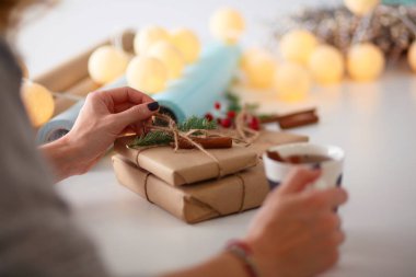 Noel hediye kutusu ile masaya oturan kadın. Kadının elleri