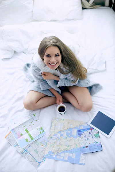 Relaxado jovem mulher sentada na cama com uma xícara de café e tablet digital — Fotografia de Stock