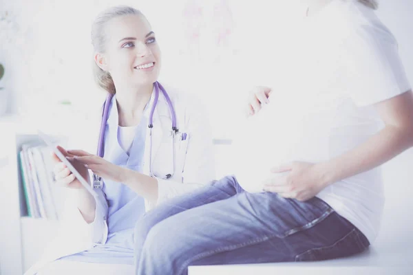 Mulher sorridente médico mostra fotos no tablet para a jovem grávida no hospital. — Fotografia de Stock