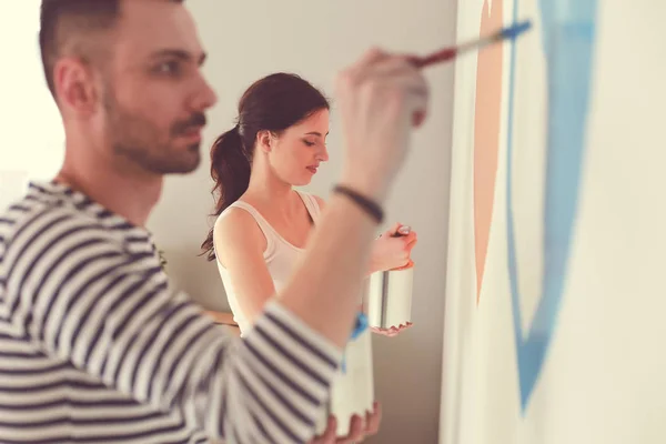 Retrato de feliz joven pareja sonriente pintando la pared interior de la casa nueva. pareja joven —  Fotos de Stock