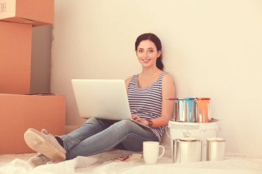 Yeni daire dizüstü bilgisayar ile oturup, boyama sırasında genç kadın portre. Dizüstü bilgisayar ile genç kadın