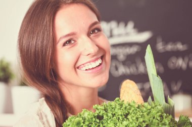 Mutfakta elinde sebzelerle gülümseyen genç bir kadın. Gülümseyen genç kadın