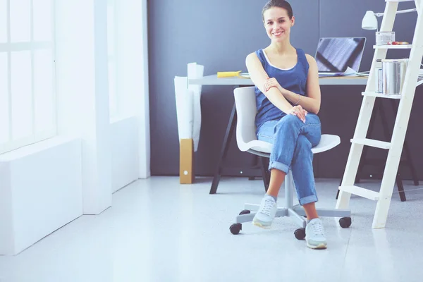 Ung kvinna sitter vid skrivbordet med instrument, plan och laptop. — Stockfoto