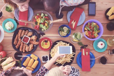 Ahşap masada otururken birlikte yemek yiyen bir grup insanın üst düzey görüntüsü. Masada yemek var. İnsanlar fast food yiyor..