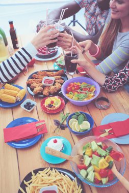 Ahşap masada otururken birlikte yemek yiyen bir grup insanın üst düzey görüntüsü. Masada yemek var. İnsanlar fast food yiyor..