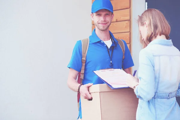 Lächelnder Zusteller in blauer Uniform liefert Paketkasten an Empfänger aus - Kurierdienst-Konzept. Lächelnder Zusteller in blauer Uniform — Stockfoto