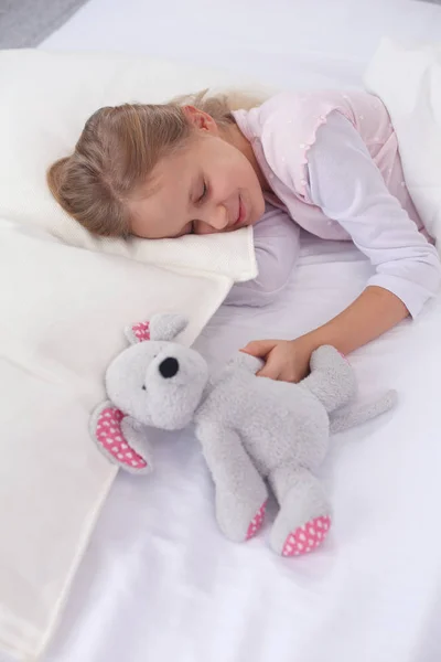 Kind meisje slaapt in het bed met een speeltje teddy beer. — Stockfoto