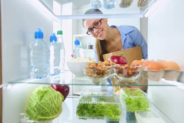 Retrato de fêmea em pé perto da geladeira aberta cheia de alimentos saudáveis, legumes e frutas. — Fotografia de Stock