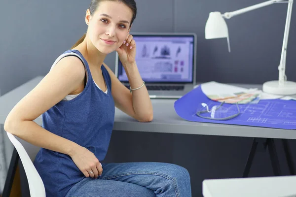 年轻妇女坐在办公桌前，手里拿着仪器、计划和笔记本电脑. — 图库照片