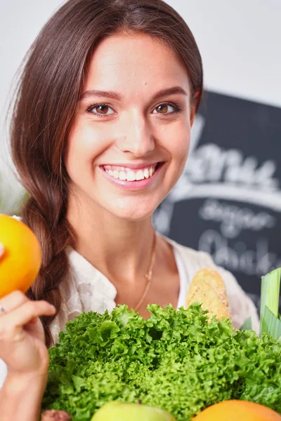 Mujer joven sonriente sosteniendo verduras de pie en la cocina. Jovencita sonriente —  Fotos de Stock