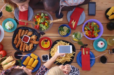 Ahşap masada otururken birlikte yemek yiyen bir grup insanın üst düzey görüntüsü. Masada yemek var. İnsanlar fast food yiyor..