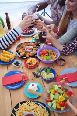 Ahşap masada otururken birlikte yemek yiyen bir grup insanın üst düzey görüntüsü. Masada yemek var. İnsanlar fast food yiyor..
