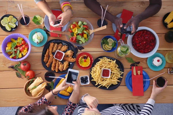 Vue du dessus du groupe de personnes qui dînent ensemble tout en étant assis à une table en bois. De la nourriture sur la table. Les gens mangent fast food. — Photo