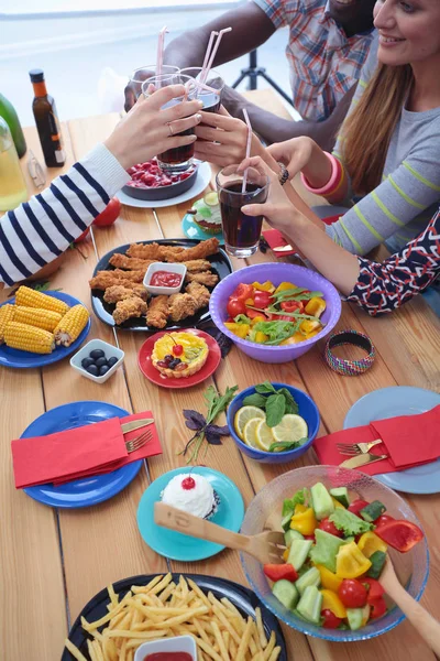 木製のテーブルに座っている間に一緒に夕食を持っている人々のグループのトップビュー。テーブルの上の食べ物。人々はファーストフードを食べる. — ストック写真