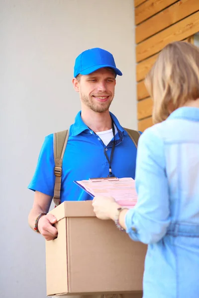 Repartidor sonriente con uniforme azul que entrega la caja de paquetes al destinatario: concepto de servicio de mensajería. Repartidor sonriente en uniforme azul — Foto de Stock