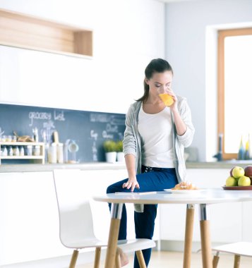 Mutfakta portakal suyu ve tableti olan genç bir kadın..