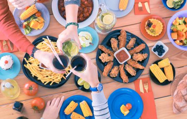 Ahşap masada otururken birlikte yemek yiyen bir grup insanın üst düzey görüntüsü. Masada yemek var. İnsanlar fast food yiyor..