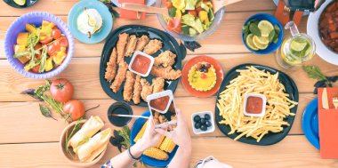 Ahşap masada otururken birlikte yemek yiyen bir grup insanın üst düzey görüntüsü. Masada yemek var. İnsanlar fast food yiyor..