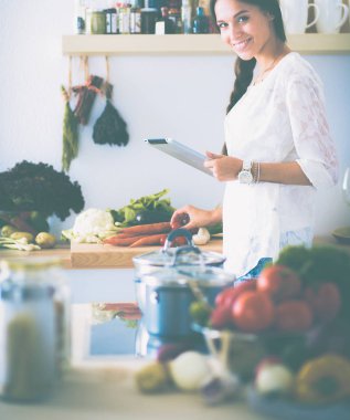 Mutfakta yemek yapmak için tablet bilgisayar kullanan genç bir kadın.