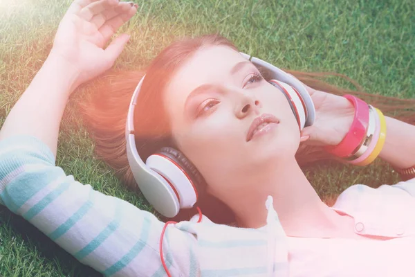 年轻女人听听音乐，躺在绿色的草地上 — 图库照片