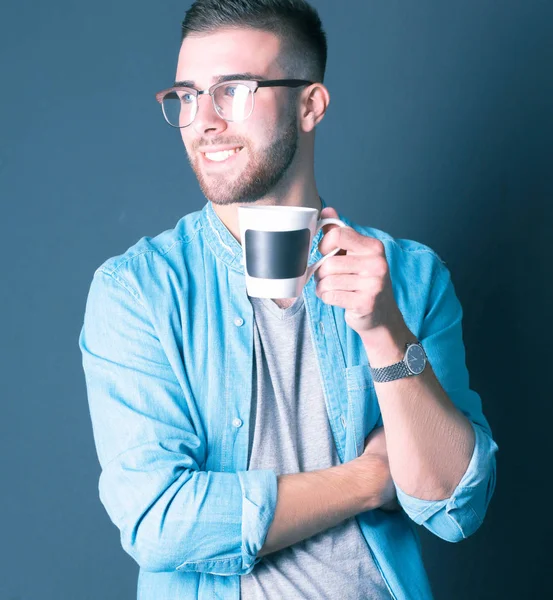 Portret van een knappe jongeman permanent en houden van een kopje koffie in zijn handen — Stockfoto