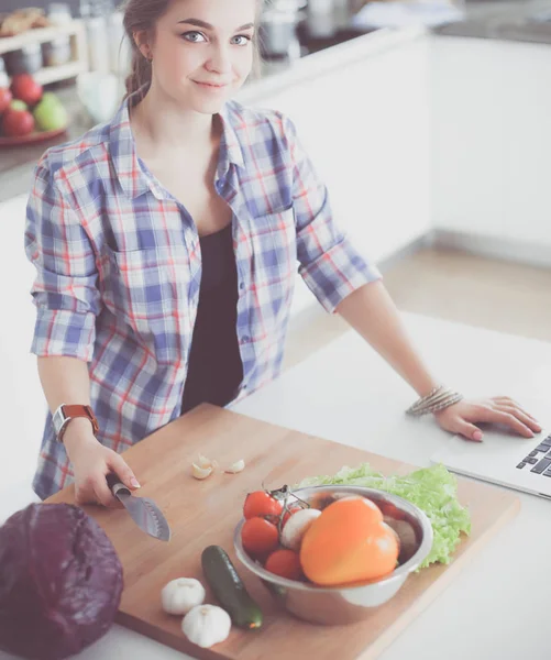 Masanın yanındaki mutfakta sebze doğrayan genç bir kadın..