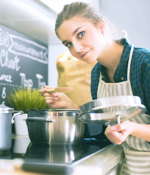 Νεαρή γυναίκα στέκεται δίπλα στη σόμπα στην κουζίνα . — Φωτογραφία Αρχείου