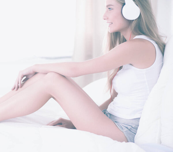 Portrait of beautiful woman in morning listening music sitting on bed at home.