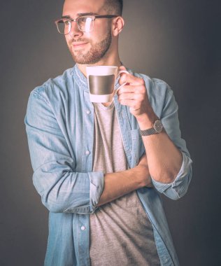 Yakışıklı bir genç adam ayakta ve bir fincan kahve onun elinde tutan portresi