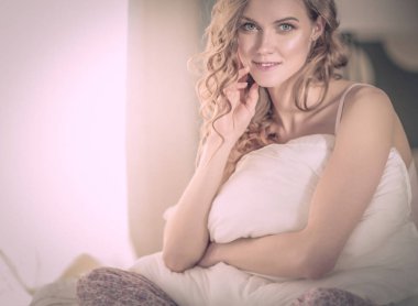 Yatağında otururken bir yastık tutan genç kadın.