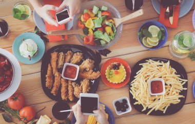 Ahşap masada otururken birlikte yemek yiyen bir grup insanın üst düzey görüntüsü. Masada yemek var. İnsanlar fast food yiyor..