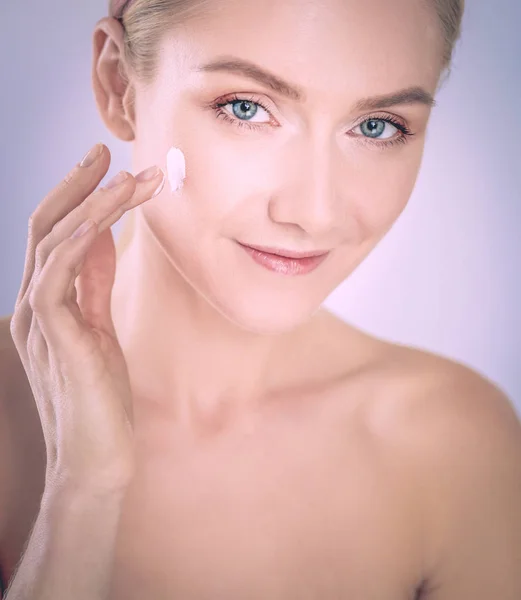 Portret van een vrolijke glimlachende mooie jonge vrouw die de huid aanraakt of crème aanbrengt, geïsoleerd over een witte achtergrond — Stockfoto