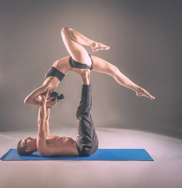 Pareja joven practicando acro yoga en estera en estudio juntos. Acroyoga. Un par de yoga. Socio yoga . — Foto de Stock