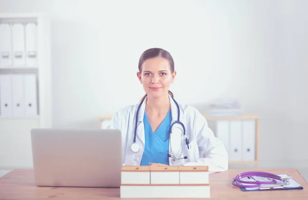 Bela jovem e sorridente médica sentada na mesa e escrevendo. médico feminino — Fotografia de Stock