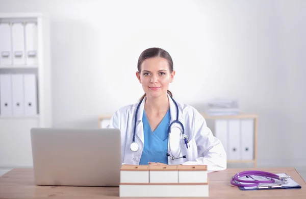 Hermosa joven sonriente doctora sentada en el escritorio y escribiendo. doctora — Foto de Stock