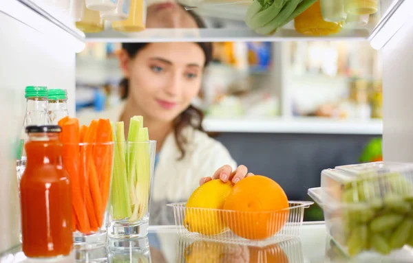 Retrato de fêmea em pé perto da geladeira aberta cheia de alimentos saudáveis, legumes e frutas. Retrato de fêmea — Fotografia de Stock