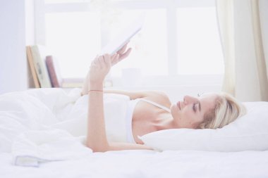 Elinde boş ekranlı dijital tablet tutan ve yatak odasında kameraya gülümseyen bir kız.