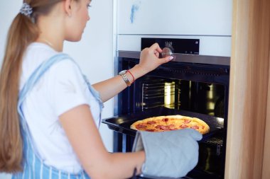 Mutlu genç bayan evde pizza pişiriyor.
