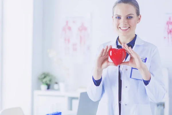 Jonge vrouw arts met een rood hart, staande op ziekenhuis achtergrond — Stockfoto