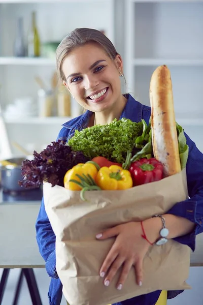 Ung kvinna som håller i matkassen med grönsaker.Står i köket — Stockfoto