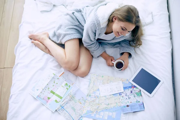 Entspannte junge Frau sitzt mit einer Tasse Kaffee und digitalem Tablet im Bett — Stockfoto